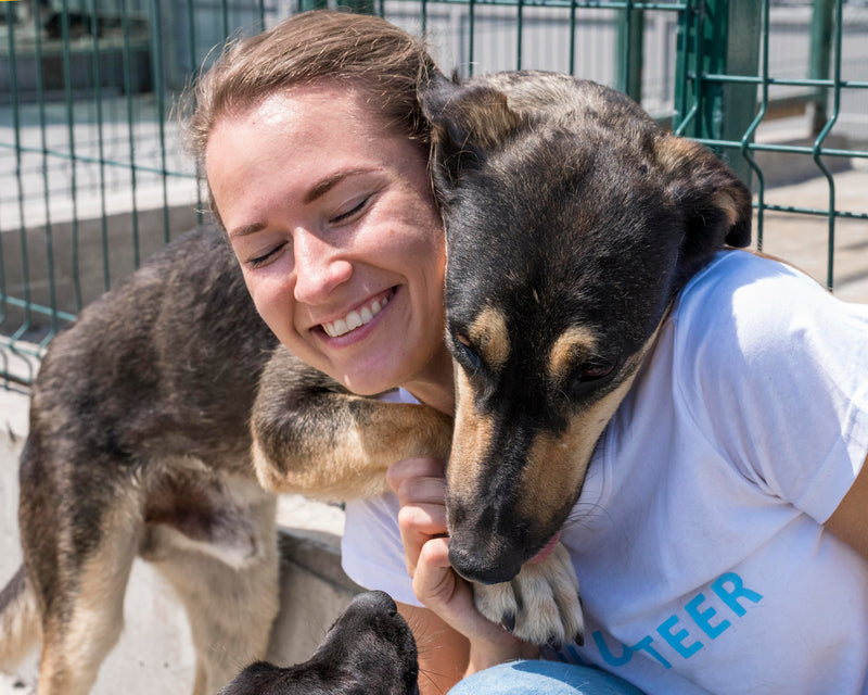 Woman in a volunteer shirt with a dog hugging each other at an animal shelter